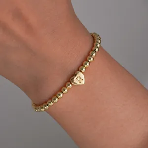 Detail of 18K gold-plated beaded bracelet with a heart charm and initial R engraving