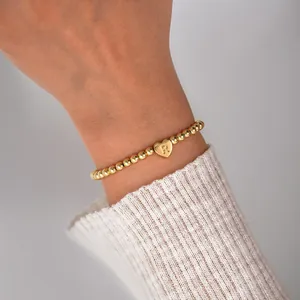 Close-up of gold beaded bracelet featuring a heart pendant with the letter R on a wrist