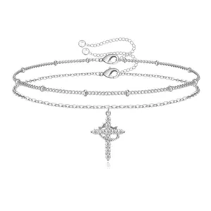 Detail of layered silver chain bracelet with zircon-encrusted cross pendant and lobster clasp