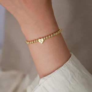 Close-up of 18K gold-plated beaded bracelet with heart charm featuring letter X on model