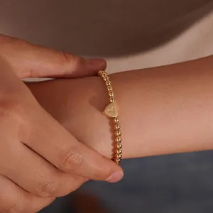 Detail of 18K gold beaded bracelet featuring a heart pendant with letter T engraving