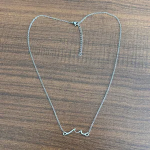 Minimalist silver wave pendant necklace with lobster clasp on a textured wooden background