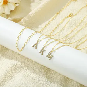 Detailed view of layered paperclip chain bracelet and zircon initial necklaces in gold