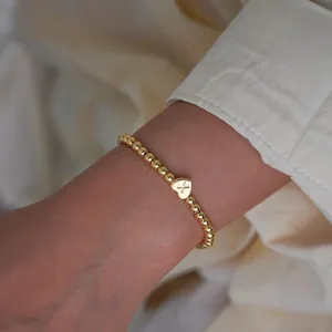 Detailed close-up of a 18K gold-plated beaded bracelet with a heart pendant engraved with X