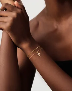 Close-up of double-layer gold chain bracelet with a sparkling zircon cross pendant