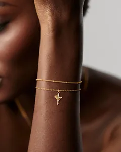 Detailed view of an 18K gold double-layer bracelet with a pavé zircon cross pendant