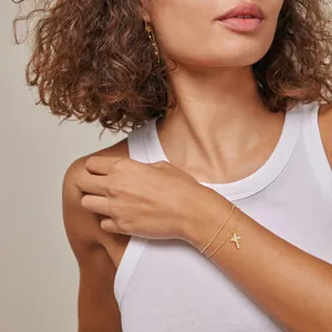 Detail of 18K gold double-layer bracelet with sparkling zircon cross charm on model