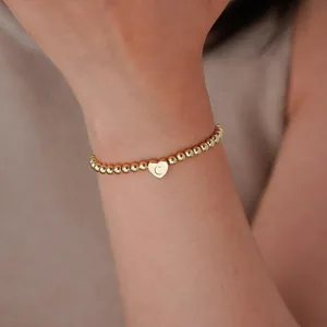 Detailed shot of 18K gold beaded bracelet with heart charm engraved with letter C
