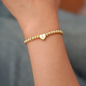 Macro shot of gold bead bracelet featuring an engraved heart charm with letter A detail