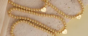Close-up of gold beaded bracelets featuring heart pendants with engraved letters T, M, J