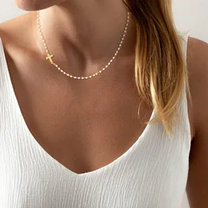 Detail of beaded necklace featuring a side-mounted gold cross pendant on a pearl chain