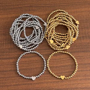 18K gold and silver beaded bracelets with heart initial charms on wood background