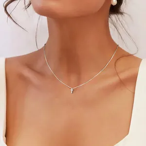 Dettaglio di un ciondolo a croce d'argento su una catena sottile indossata da una modella