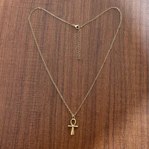 Dettaglio del ciondolo croce Ankh dorata con catena sottile su fondo in legno scuro