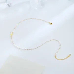 Close-up of 18K gold-plated cross pendant on a delicate white pearl chain necklace