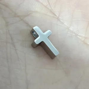Primo piano di un piccolo ciondolo a croce in acciaio inossidabile lucido sulla mano