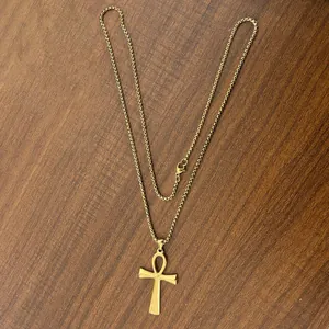 Collana dorata con ciondolo a croce Ankh e chiusura a moschettone su sfondo di legno