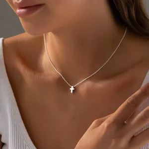Dettaglio macro della collana con pendente a croce d'argento indossata su top bianco