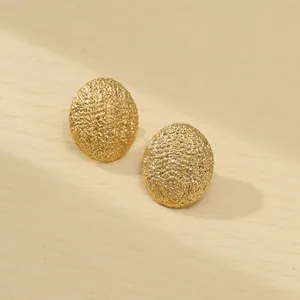 Detailed macro view of gold oval stud earrings with matte frosted metal texture