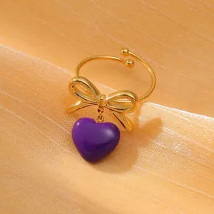 Dettaglio dell'anello con fiocco dorato e ciondolo a cuore in smalto viola su seta