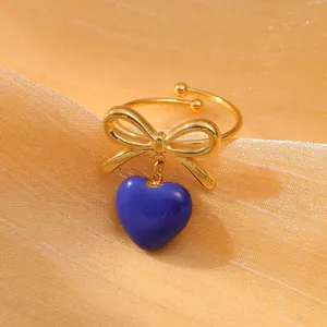 Dettaglio anello dorato con fiocco e ciondolo a cuore in smalto blu su oro
