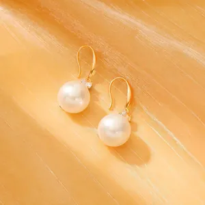 Detail of elegant gold hook earrings with white pearls and sparkling cubic zirconia