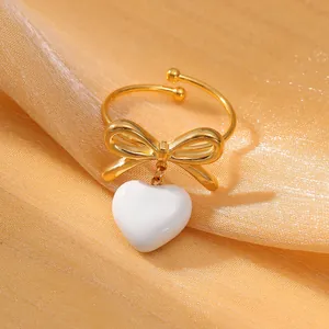 Vista dettagliata dell'anello a fiocco dorato con ciondolo a cuore bianco su seta elegante