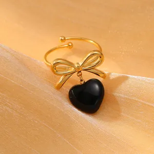 Dettaglio dell'anello dorato con fiocco e ciondolo a cuore nero su seta lucida