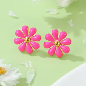 Gros plan de boucles d'oreilles marguerites roses avec centres dorés sur fond vert doux
