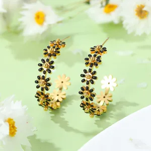 Boucles d'oreilles créoles marguerites dorées avec émail noir sur un fond floral frais