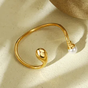 Detailansicht eines unregelmäßigen goldenen Stahlarmreifs mit Wassertropfen und Perle