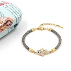 Détail macro du bracelet en cuir tressé avec breloque main de Hamsa dorée et œil bleu