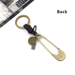 Vintage bronze safety pin keychain with brown leather wrap and metallic tags on white background