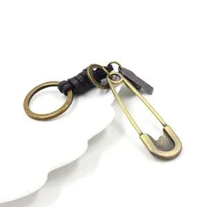 Retro safety pin keychain with brown leather wrap and engraved metal charm on white tray