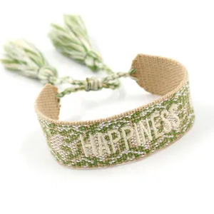 Detail of hand-woven bracelet with HAPPY embroidery and green white cotton tassels