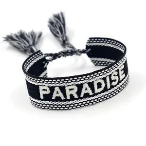 Close-up of black woven bracelet featuring white PARADISE embroidery and tassels