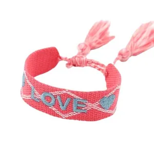 Close-up of pink woven friendship bracelet with blue LOVE embroidery and tassels