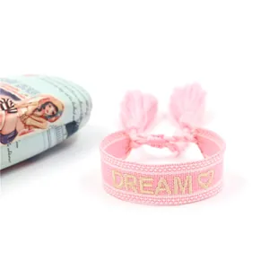 Dettaglio del bracciale dell'amicizia in tessuto rosa con ricamo DREAM dorato e nappe