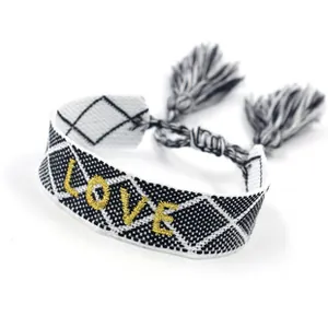 Dettaglio del ricamo dorato LOVE su bracciale intrecciato bianco e nero con nappe
