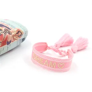 Dettaglio del bracciale rosa intrecciato con ricamo DREAM dorato e piccole nappe