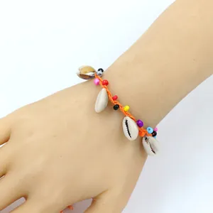 Detail eines böhmischen gewebten Armbands mit Kaurimuscheln und bunten Perlen am Handgelenk