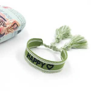 Detail of hand-woven green and white bohemian bracelet with Happy embroidery and tassels