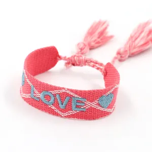 Pink woven friendship bracelet with blue LOVE embroidery and tassel detail in boho style
