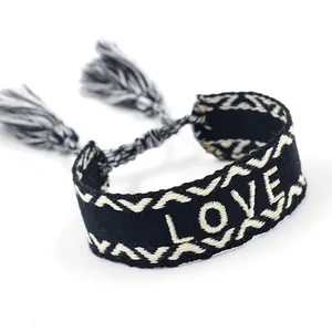 Detalle de pulsera de la amistad tejida con texto LOVE blanco y borlas