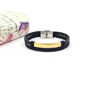 Detalle de una pulsera multicapa de cuero trenzado negro con placa de metal dorado pulido