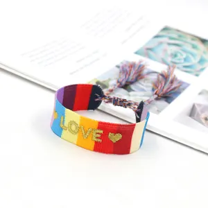 Detailansicht eines Regenbogen-Webarmbands mit goldener LOVE-Stickerei und bunten Quasten