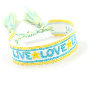 Detail eines gewebten Boho-Freundschaftsarmbands mit LIVE LOVE Stickerei und Quasten