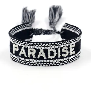 Detail der PARADISE Stickerei auf schwarz-weißem gewebtem Quastenarmband