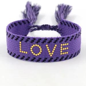 Macro detail of purple woven friendship bracelet featuring yellow LOVE lettering and tassels