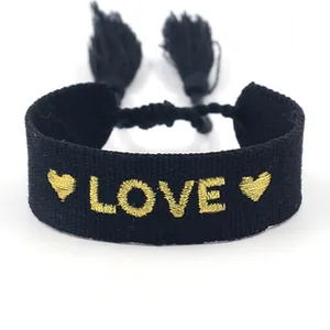 Close-up of black woven bracelet with gold LOVE embroidery and fringe tassel detail